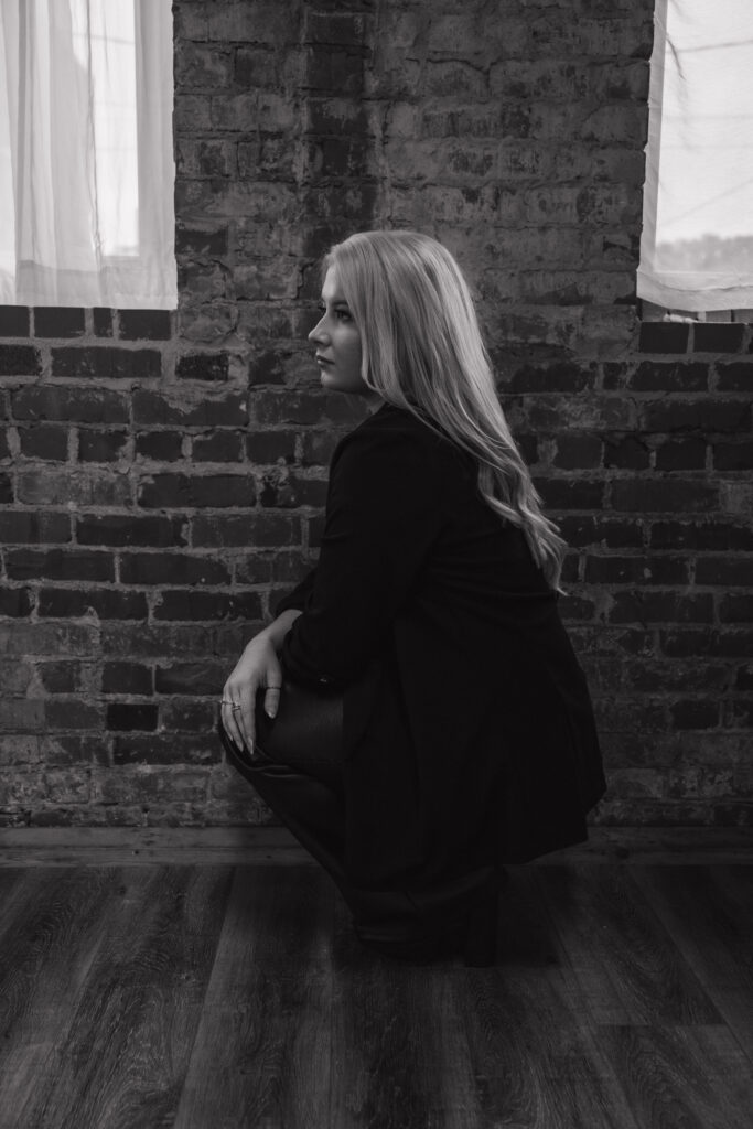 A BLACK AND WHITE PHOTO OF A BLONDE WOMAN CROUCHING INFRONT OF A BRICK WALL